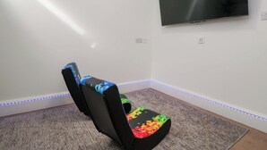 Una habitación con una televisión de pantalla plana montada en la pared, un sillón informal con estampados coloridos e iluminación LED a lo largo del zócalo.