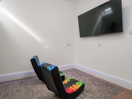 A room with a flat-screen TV mounted on the wall, a bean bag chair with colorful patterns, and LED strip lighting along the baseboard.