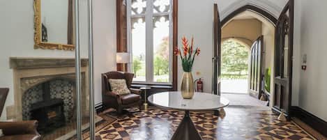 Un hall d’entrée avec un sol à motifs, une cheminée, une table ronde ornée d’un vase, une chaise et un lustre.