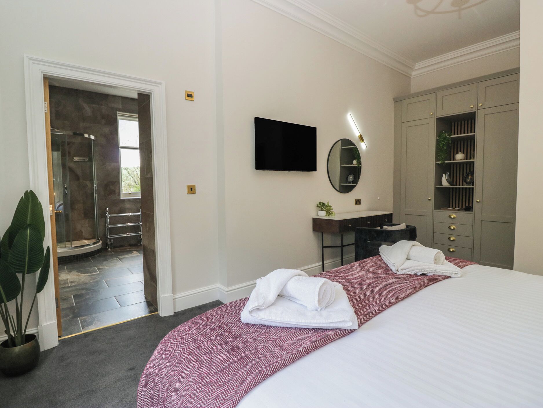 Et hotelværelse med seng, fjernsyn, spejl, skrivebord og brusekabine.