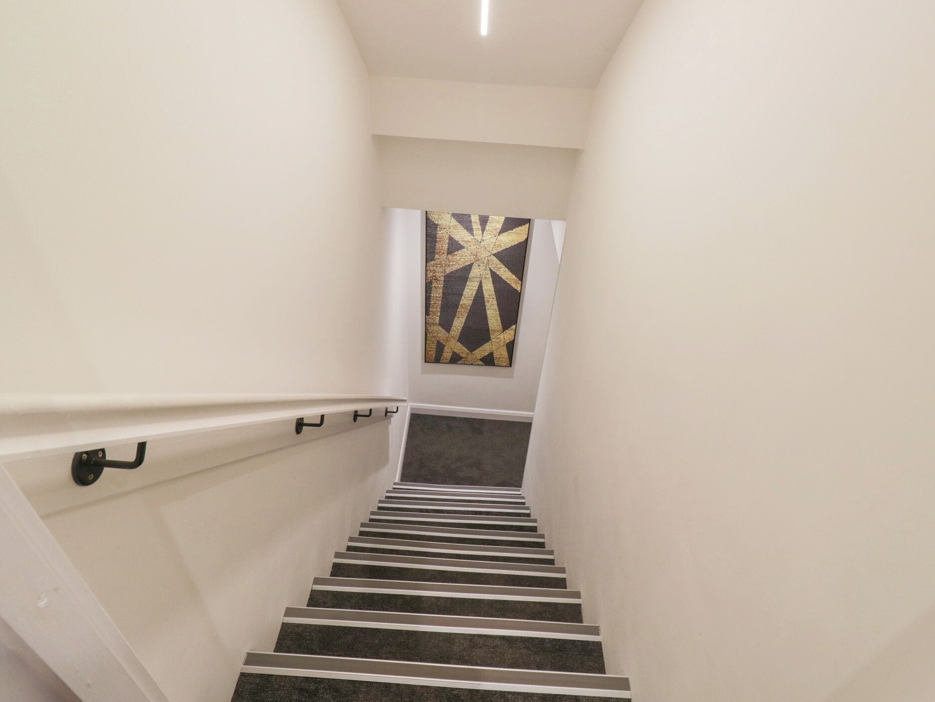 A staircase with a handrail, carpeted steps, and a wall-mounted artwork.