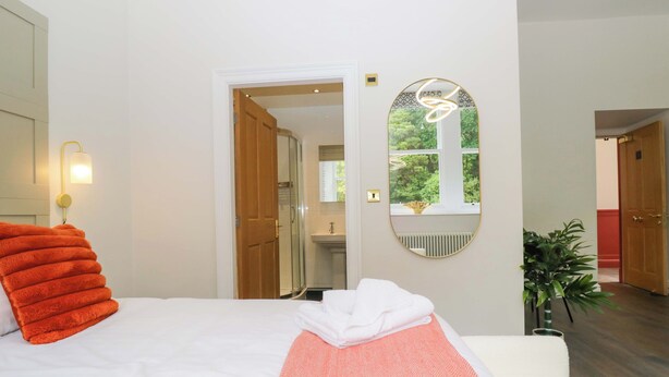 Habitación de hotel con cama, espejo, planta en maceta y vista al baño.