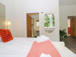 A hotel room with a bed, a mirror, a potted plant, and a view of the bathroom.