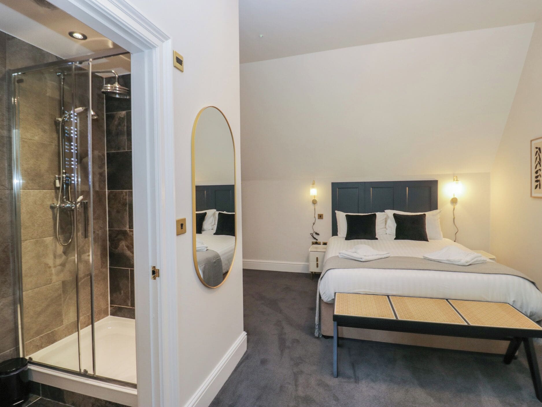 A hotel room with a shower, a bed with a headboard, a bedside table, and a bench.
