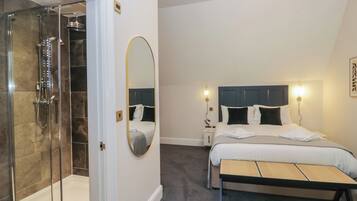 A hotel room with a shower, a bed with a headboard, a bedside table, and a bench.