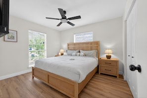 Ein Schlafzimmer mit einem Bett, zwei Nachttischen, einem Deckenventilator und zwei Fenstern mit Jalousien.