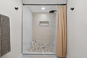 Eine Dusche mit Glastür, ein gefliestem Boden und ein kleines gerahmtes Bild an der Wand.