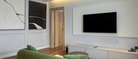 Un salon moderne avec un canapé vert, un téléviseur à écran plat fixé au mur et une porte en bois.