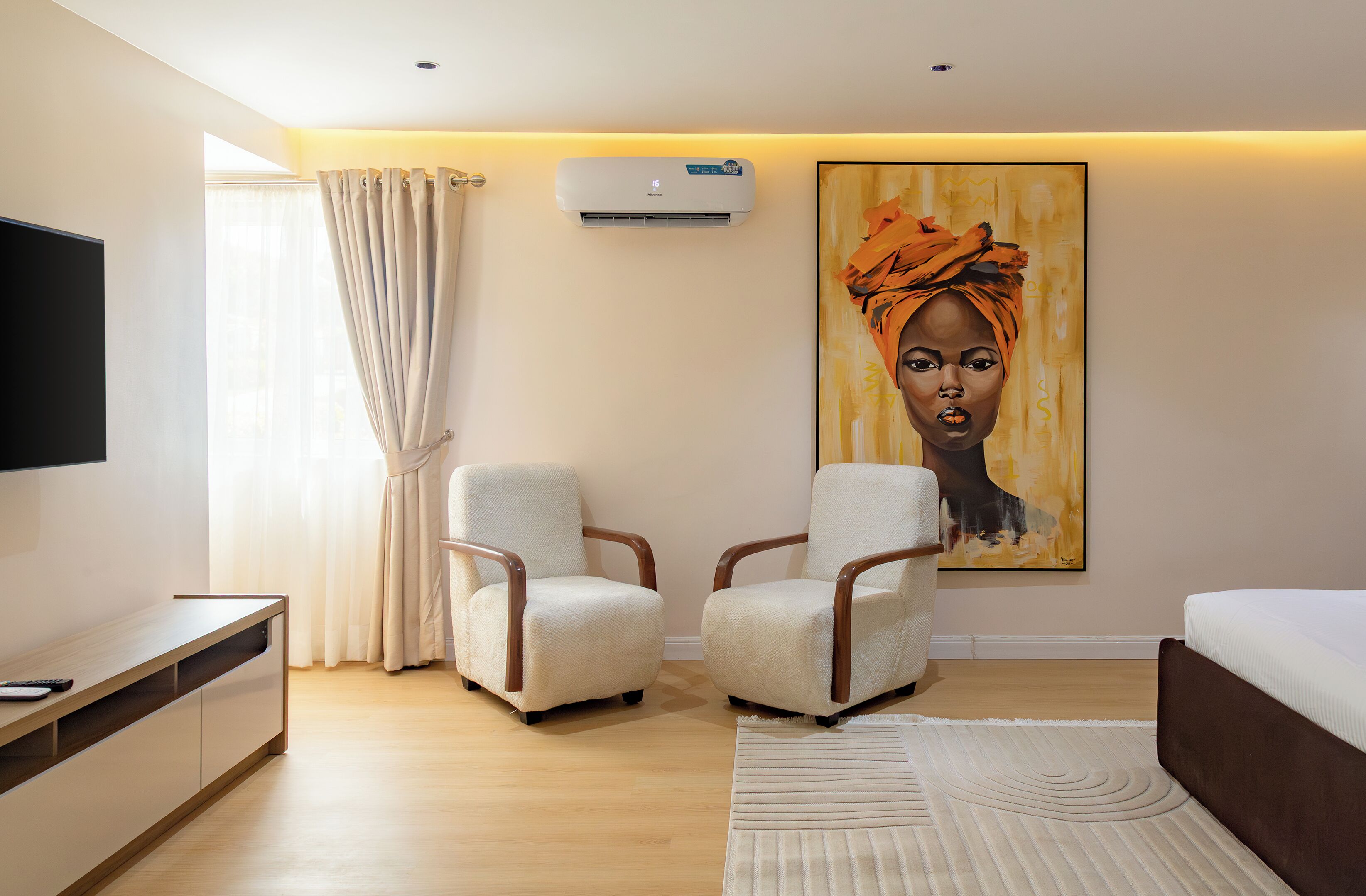 Una habitación de hotel moderna con televisión de pantalla plana, dos sillones, una cama, un cuadro grande y un equipo de aire acondicionado.