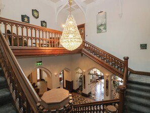 Una imponente escalera con candelabro, arcos y piso a cuadros.