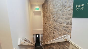 A staircase with a stone wall, an exit sign, and a sign indicating rooms 17-23.