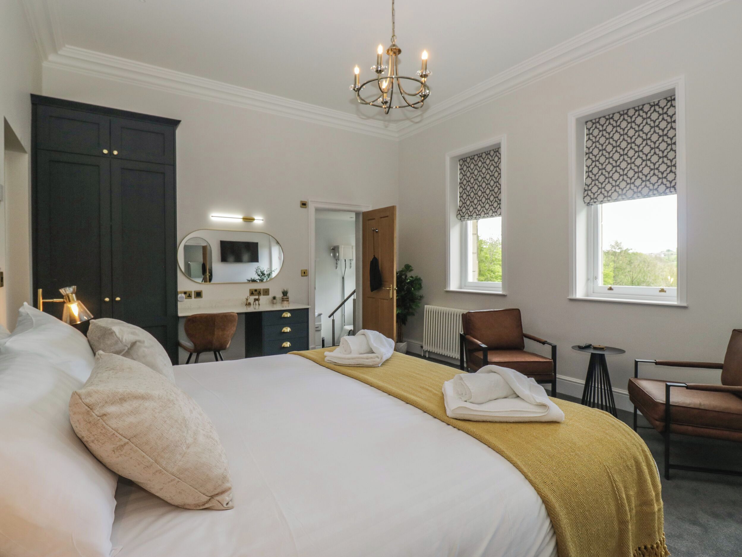 Habitación de hotel con una cama grande, un escritorio con espejo, una silla, un radiador y una ventana con vistas.