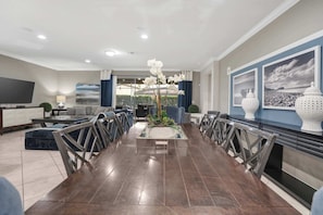 A modern living room with a dining area, a flat-screen TV, and a large window with curtains. - 6BR family retreat w/ private pool & grill (Kissimmee)