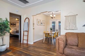 A living room with a brown sofa, wooden flooring, a dining area with yellow chairs, and a hallway with a ladder and a plant. - North Park Retreat - Hot Tub, Fire Pit & Patio (San Diego)