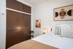 A bedroom with a bed, a nightstand, a lamp, a wall art piece, and a wardrobe. - North Park Retreat - Hot Tub, Fire Pit & Patio (San Diego)