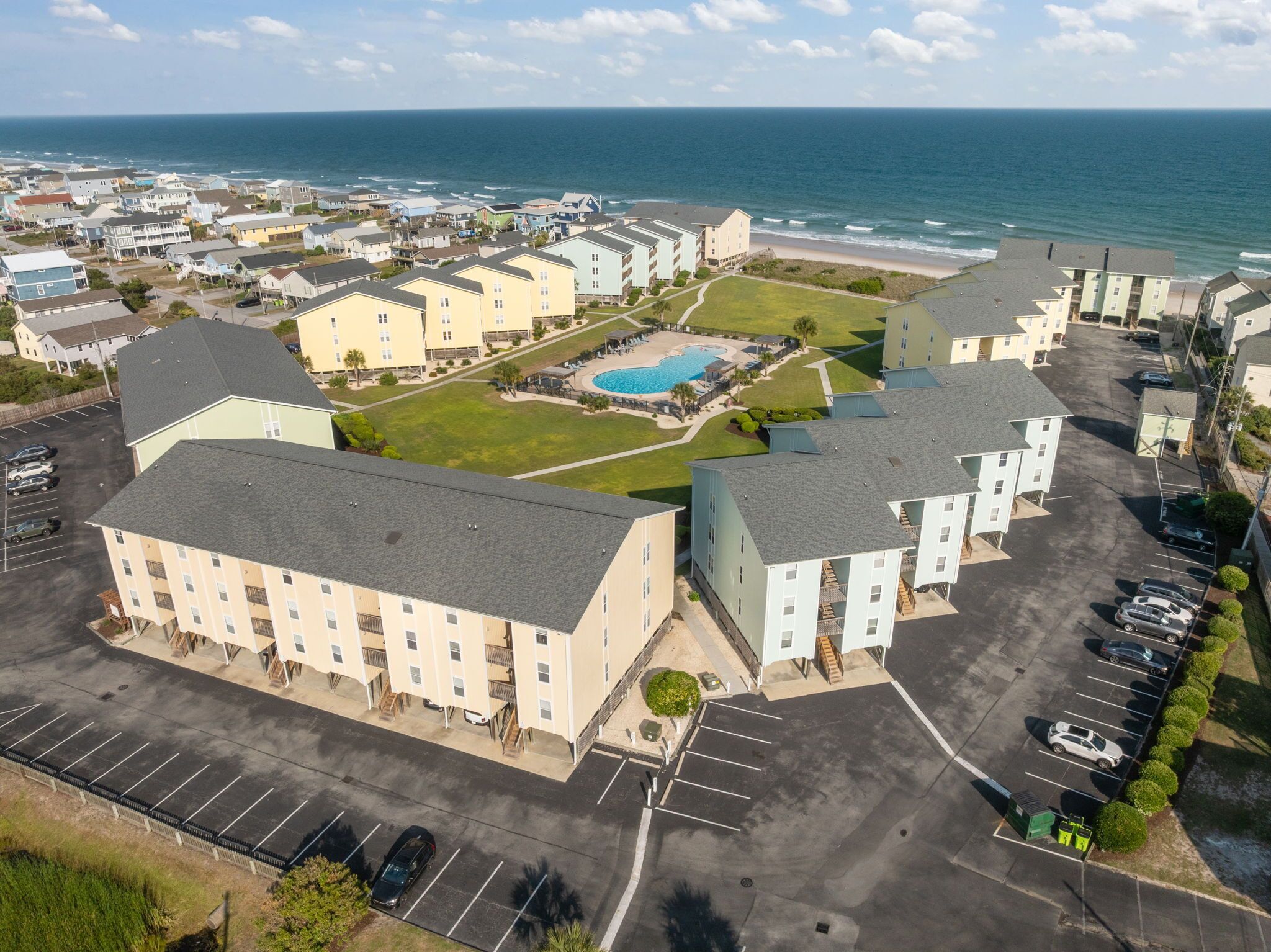 A coastal hotel with multiple buildings, a swimming pool, and a parking lot.
