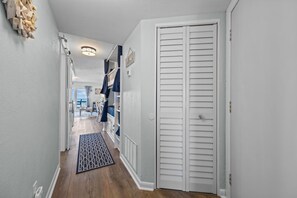 A hallway with a white door, a patterned rug, and a ceiling light fixture. - Oceanview + Beach Access w/ Pool | Driftwood Dunes (Surf City)
