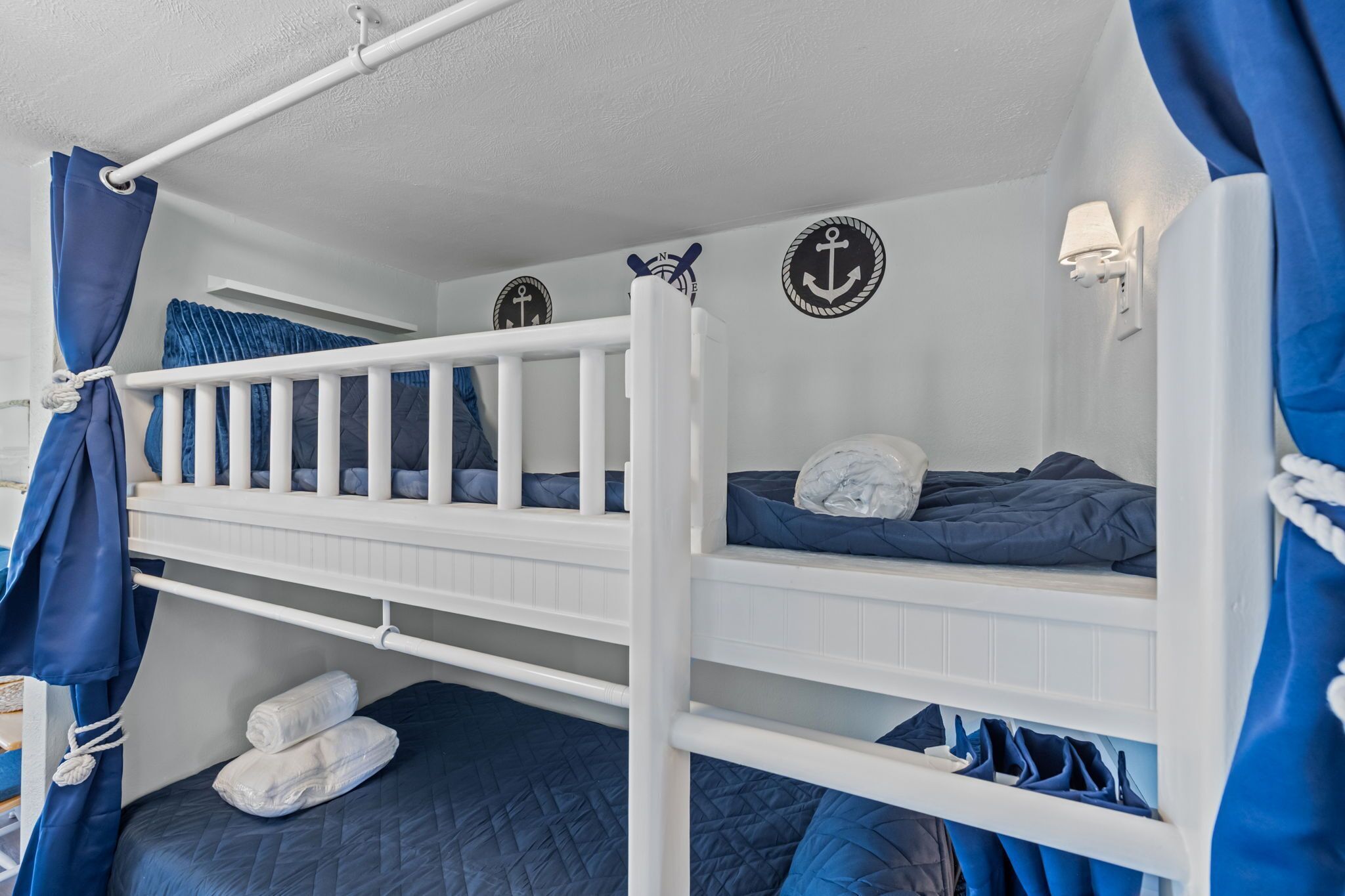 Een slaapkamer met een stapelbed, een witte spijl, marineblauwe beddengoed en decoratie met een nautisch thema.