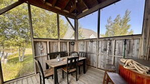 A wooden deck with a table and chairs, a bar area, and a view of trees and a house. - Coastal Lines Retreat Ocean Views Sleeps 9 (Cocagne)