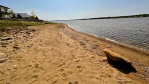 A sandy beach with a large rock, a body of water, and a building in the background. - Coastal Lines Retreat Ocean Views Sleeps 9 (Cocagne)