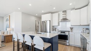Une cuisine moderne dotée d’un îlot central, d’appareils électroménagers en acier inoxydable et de meubles blancs.
