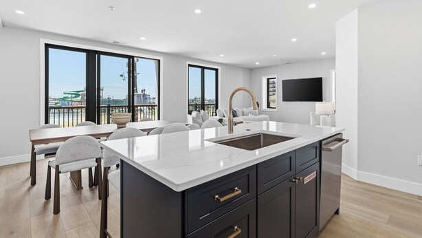 Une cuisine moderne dotée d’un grand îlot central, de meubles de rangement aux couleurs sombres et d’un coin repas avec une table et des chaises.