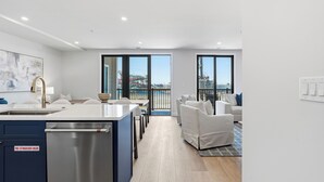 Une cuisine moderne équipée d’un lave-vaisselle intégré, un coin repas avec une table et des chaises blanches, et un balcon avec vue sur un parc aquatique.