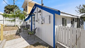 Ein kleines, einstöckiges Haus mit blauer Akzentwand, einer Veranda mit zwei Stühlen und einem weißen Zaun.
