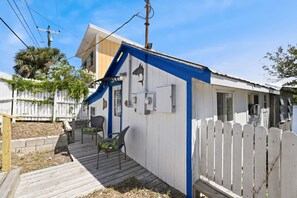 A small, single-story house with a blue accent wall, a porch with two chairs, and a white picket fence.