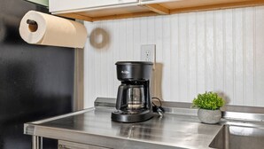 Eine Küche mit Kaffeemaschine, Küchenpapierrolle, Blumentopf und Spüle aus Edelstahl.