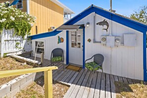 A small, single-story building with a blue roof and white walls, featuring a porch with two chairs and a small table.