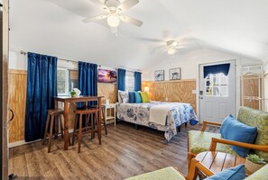 A room with a bed, a desk, chairs, a ceiling fan, and a door.