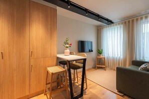 Una sala de estar moderna con un sofá, una mesa de comedor con sillas, un televisor y un amplio armario de madera.