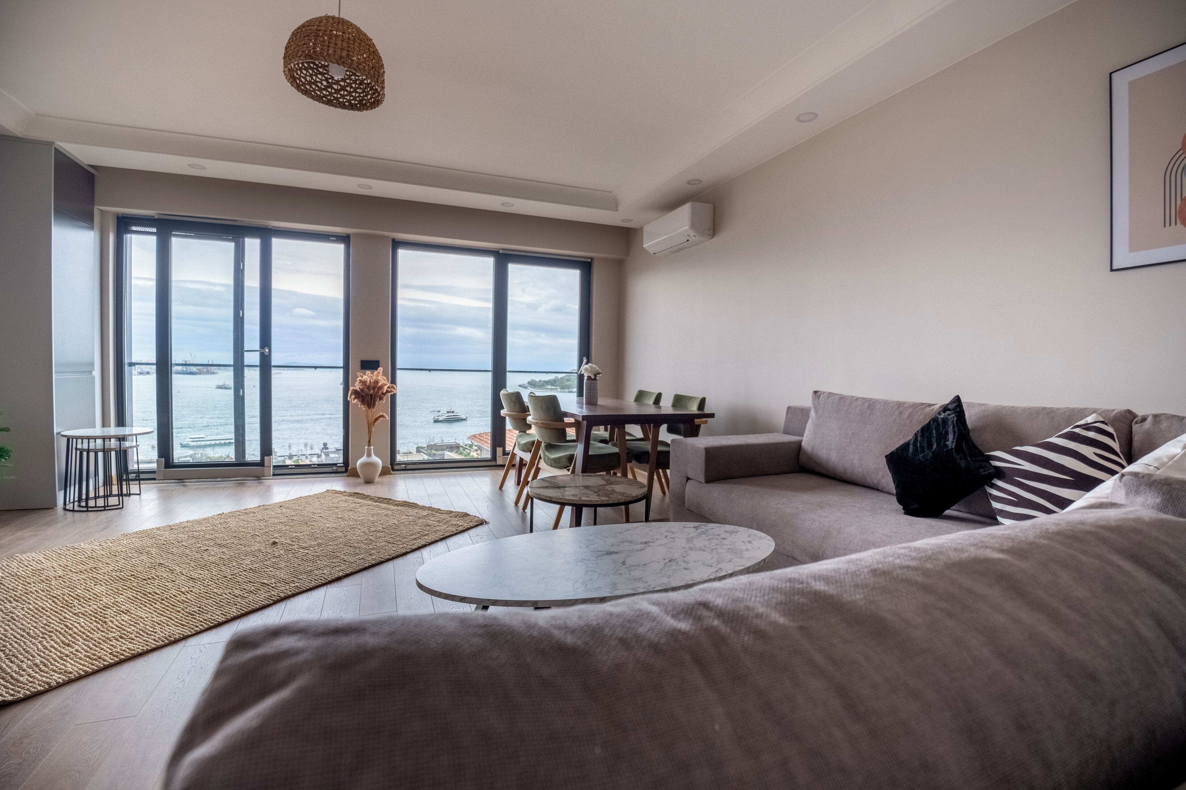 A modern living room with a large window, a sofa, a round coffee table, and a dining area.