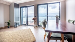 A modern dining area with a large table, chairs, and a view of the sea through large glass doors. - Bosphorus View 2BR Luxury Apartment - Parking & Elevator (İstanbul)