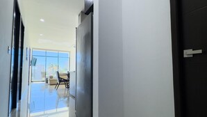 A hallway with a glass door leading to a room with a sofa and chairs, a dark door on the right, and a ceiling with recessed lighting. - Golden Zone Escape: Stylish New Condo Steps from the Beach & Everything You Love (Mazatlan)