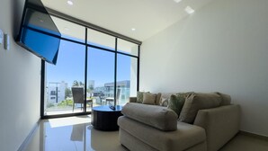 A modern living room with a sofa, a round coffee table, and a TV mounted on the wall. - Golden Zone Escape: Stylish New Condo Steps from the Beach & Everything You Love (Mazatlan)