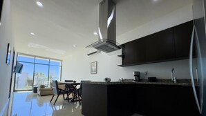 A modern kitchen with a large island, dark cabinetry, and a view of the city through large windows. - Golden Zone Escape: Stylish New Condo Steps from the Beach & Everything You Love (Mazatlan)
