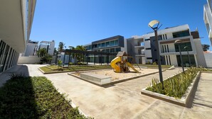 A modern building with a courtyard, a yellow play structure, and a street lamp. - Golden Zone Escape: Stylish New Condo Steps from the Beach & Everything You Love (Mazatlan)