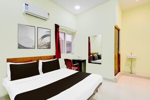 Ein Hotelzimmer mit einem Bett, einem Schreibtisch, einem Stuhl, einer Klimaanlage, einem Fenster mit Vorhängen, einem Spiegel und einem Waschbecken.