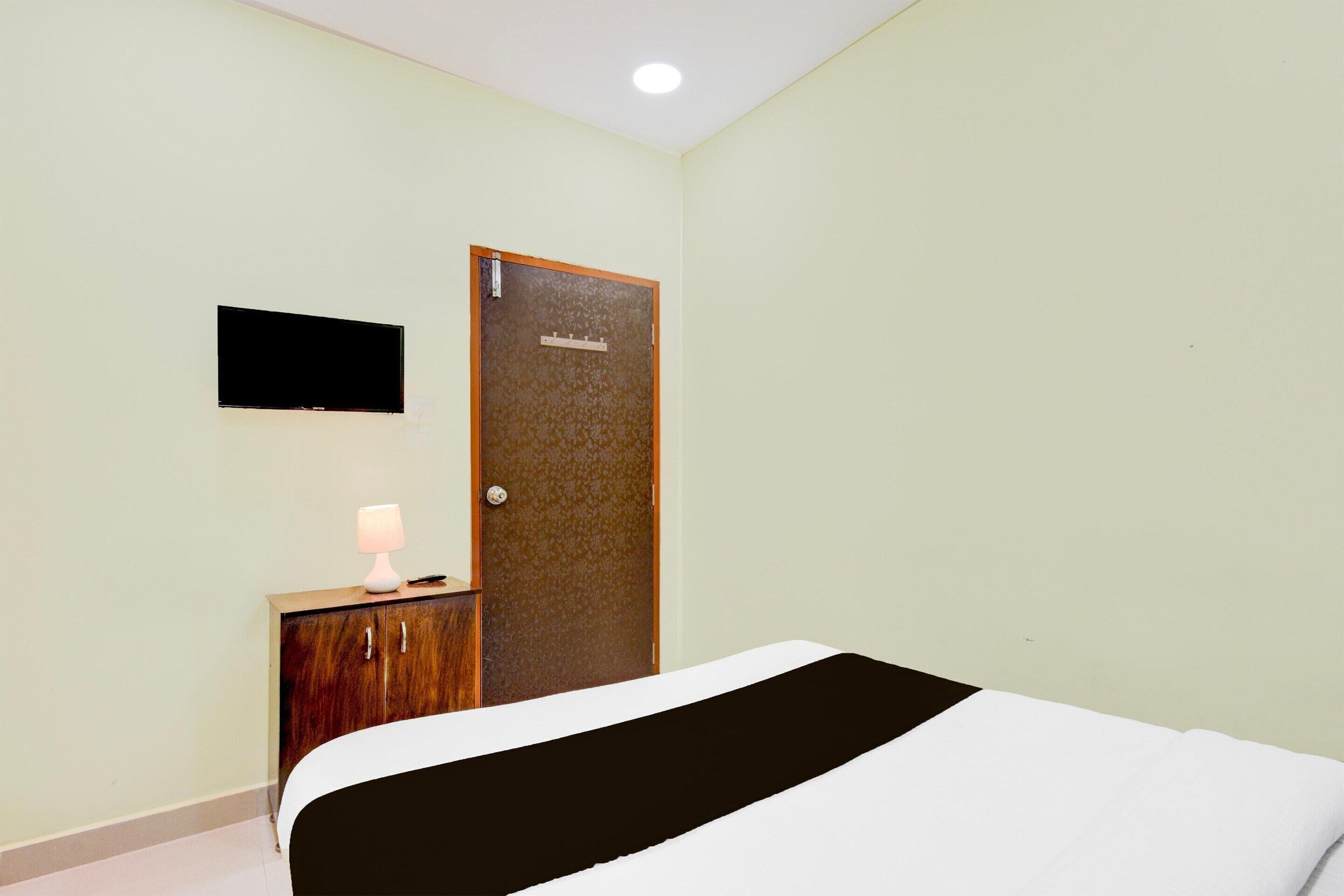 A hotel room with a bed, a small wooden cabinet with a lamp, and a door with a sign.