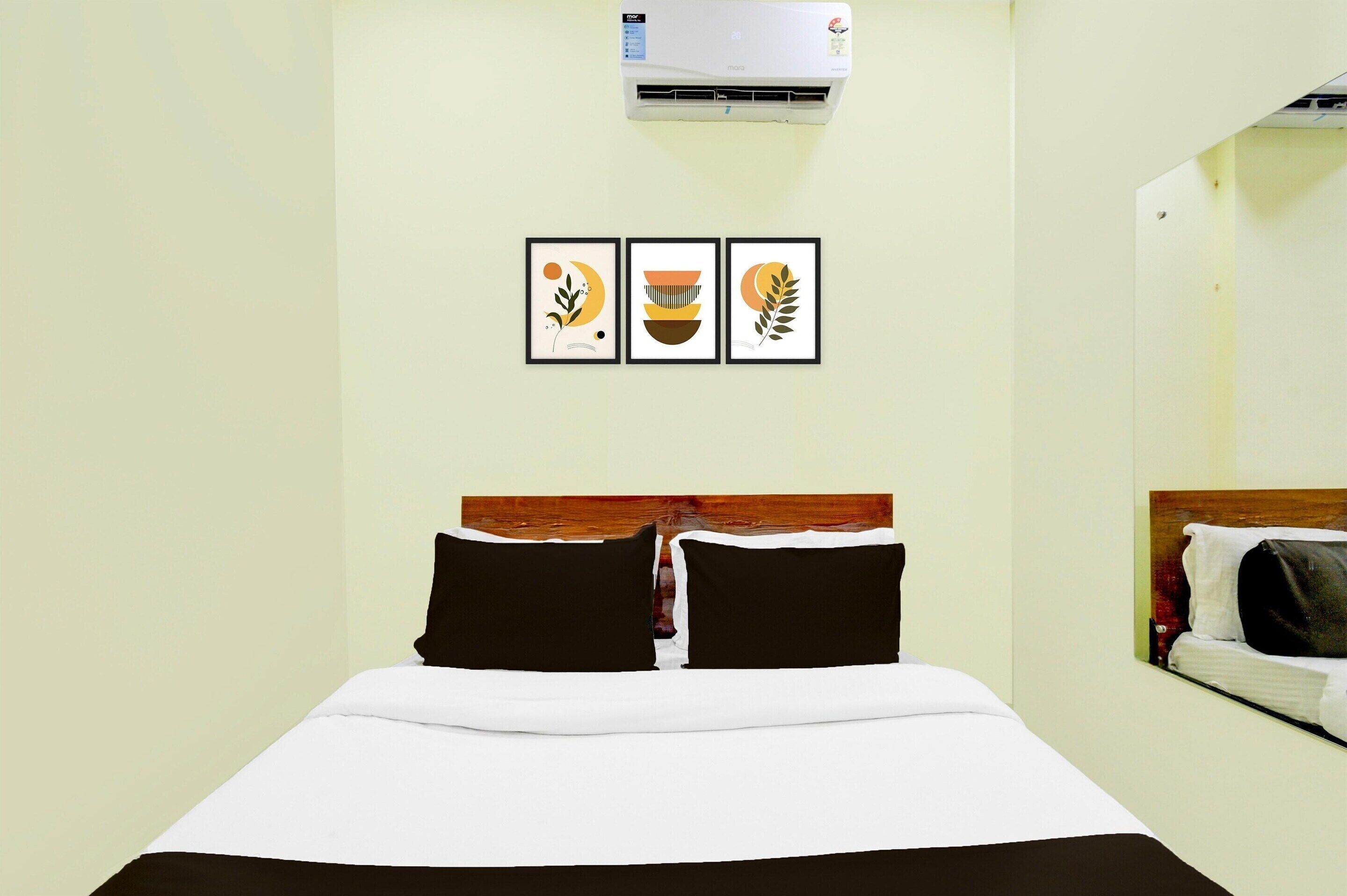 Ein Hotelzimmer mit einem Bett, einer wandmontierten Klimaanlage und drei gerahmten Kunstwerken über dem Bett.