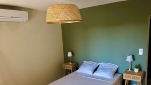 A neatly made bed with white linens, two bedside tables with lamps, a woven hanging light fixture, and an air conditioning unit on the wall. - Magnificent Bastide with swimming pool in the heart of nature (Puéchabon)