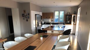 A modern kitchen with a central island, white chairs, and a wooden dining table. - Magnificent Bastide with swimming pool in the heart of nature (Puéchabon)