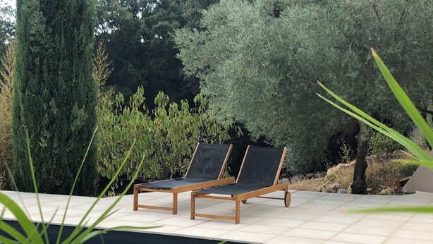 A poolside area with two wooden lounge chairs and a tiled deck. - Magnificent Bastide with swimming pool in the heart of nature (Puéchabon)
