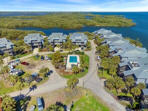An aerial view of a coastal resort with multiple buildings, a central swimming pool, and surrounding water bodies.