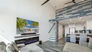 Ein modernes Wohnzimmer mit Flachbildfernseher, Kamin und einer Treppe, die zur Küche führt.
