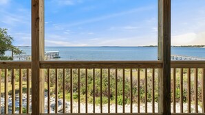A wooden deck with a view of a calm body of water, a dock, and distant land.