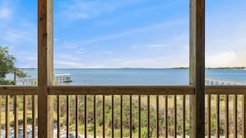 A wooden deck with a view of a calm body of water, a dock, and distant land.