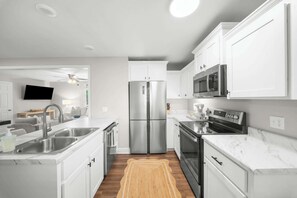 A modern kitchen with white cabinets, stainless steel appliances, and a wooden floor. - GSU Getaway, 4BR3BA, spacious pet friendly (Statesboro)